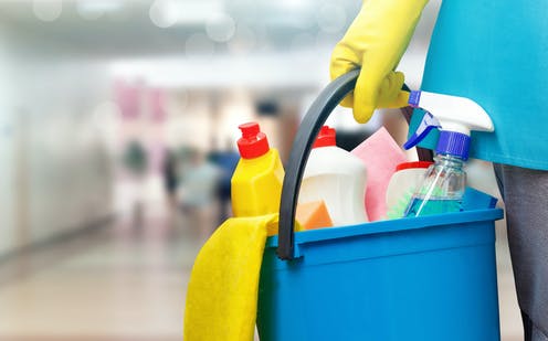 Cleaner holding a blue caddy filled with cleaning sprays, cloths and supplies